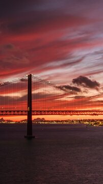 Time-lapse of 25 de Abril Bridge famous tourist landmark of Lisbon connecting Lisboa and Almada on Setubal Peninsula over Tagus river in the evening twilight. Lisbon, Portugal. Zoom out effect