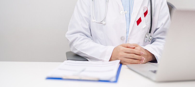 doctor using laptop and report notes on notebook. Burgundy and white ribbon to patient for concept of April Oral, Head and Neck Cancer Awareness month, Healthcare and February world cancer day