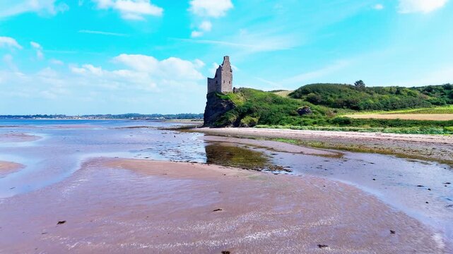 Greenan Castle at Ayr, Scotland, revealing the historic coastal ruin above a sandy beach, farmland and the Firth of Clyde, dolly forward aerial view