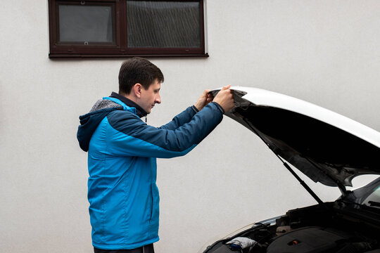 Auto repair and routine vehicle service concept. A driver opens the hood of a white car outdoors to check the engine status and perform routine maintenance