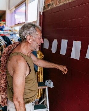 Halloween retail display planning by a man arranging blank price talkers on a burgundy brick wall for a costume store mockup