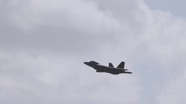 Modern stealth fighter jet flies through cloudy sky.