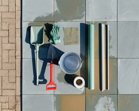 Drain cleaning kit with a metal bucket and tools laid out on a wet stone surface, utilitarian arrangement for maintenance and repair