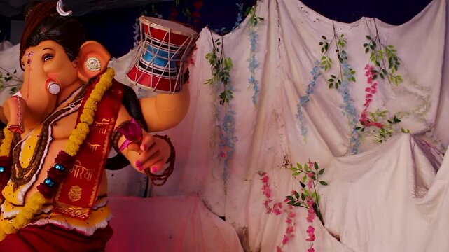 Ganesh idol close up dressed as Lord Shiva holds trishul and prayer beads, marigold garlands and Ganpati Bappa Morya sash, festival celebration India.