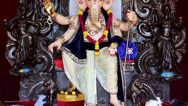 India Ganesh Chaturthi pandal shows close up tilt shot of Lord Ganesha idol adorned with garlands, jewelry and gold ornaments during Hindu festival.