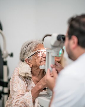 Senior South Asian patient undergoing an eye screening with a glowing autorefractor for health care and prevention in a clinic