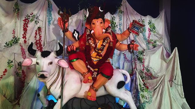 Ganesh idol dressed as Lord Shiva sits on Nandi bull holding trishul, green ambient light and floral drapes decorate pandal during Ganesh Chaturthi India.