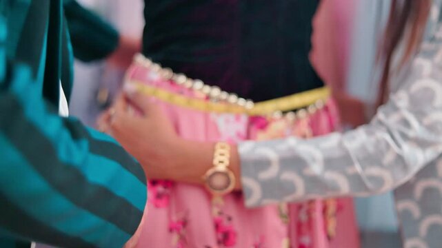 Close up shot of a female and male fashion designer measuring the waistline of a floral skirt on a mannequin during garment design work.
