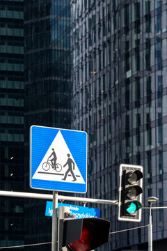Traffic signal and pedestrian bicycle crossing sign against modern office buildings, showing urban mobility infrastructure in a dense business district