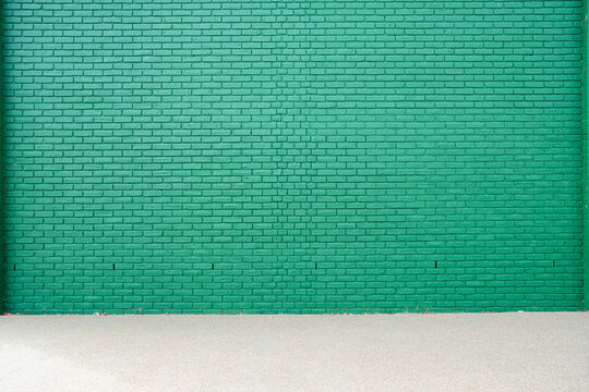 Minimalist green brick wall beside an empty urban walkway, creating a graphic architectural background within a quiet pedestrian environment