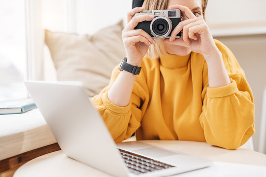 Female photographer taking a photo with camera while working on laptop