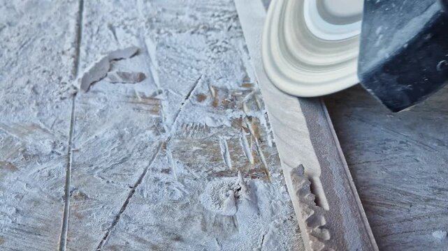 The process of cutting or grinding tiles with an angle grinder at a construction site. Close-up of a rotating diamond disc of a grinder, dust formation during construction and repair work.