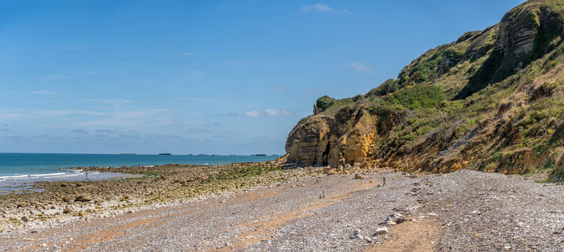 Longues-sur-Mer, France - 08 10 2026: Panoramic view of the pebble beach with cairns surrounded by cliffs, sea and pontoons with blue sunny sky