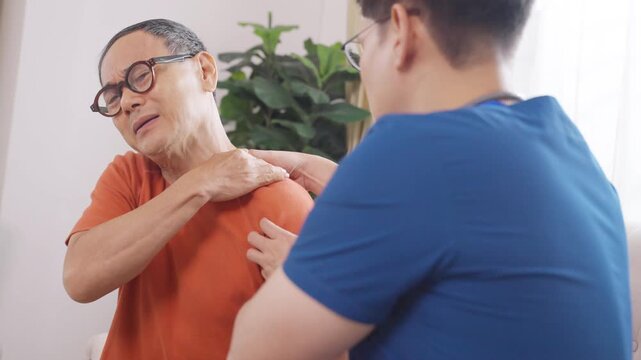 Asian senior man receiving shoulder and neck pain treatment from physical therapist at home, physiotherapy rehabilitation for elderly patient recovery, healthcare muscle therapy pain relief care
