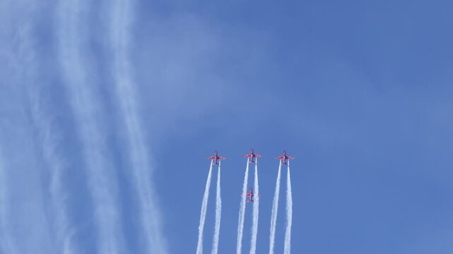 Four red aerobatic planes performing synchronous loop stunts with white smoke trails against clear blue sky in morning.
