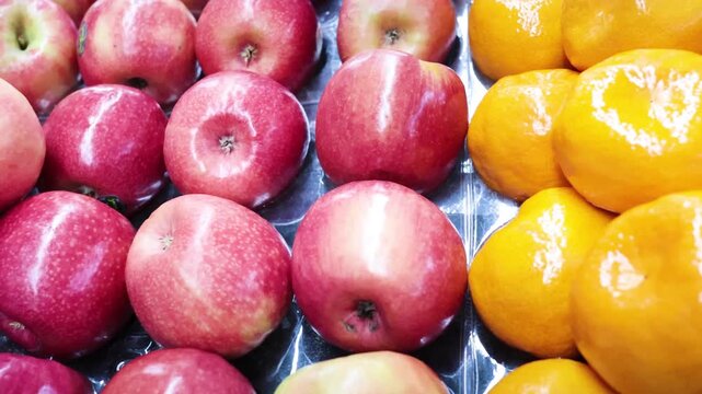 Rows of fresh red apples transitioning to bright oranges in produce display cinematic motion.