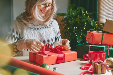 Obraz premium Woman wrapping Christmas gifts at home. Preparing presents for loved ones reflects holiday shopping, seasonal celebrations, gift giving and the joy of Christmas traditions.