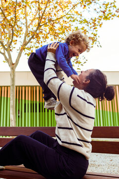 Mother lifting laughing child in the air while playing outdoors, embracing the bond and happiness of family