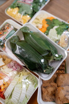 Colorful takeaway style trays hold fresh vegetables, wrapped greens, mushrooms, tofu, and mixed side dishes, viewed from above on soft warm background for catering, delivery, and meal planning