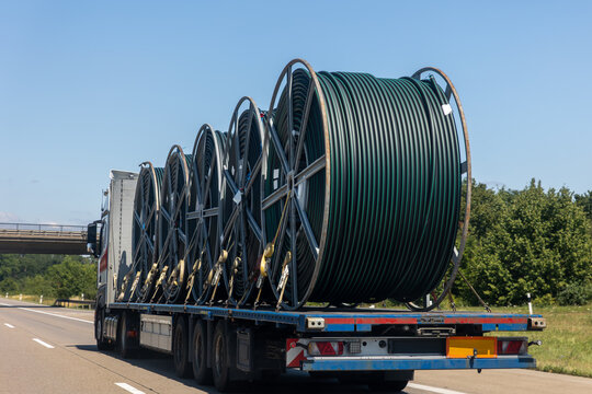 Heavy truck transports large cable reels along highway under clear blue sky. Industrial cargo of coiled tubing supports infrastructure, utility, construction and logistics projects across Europe