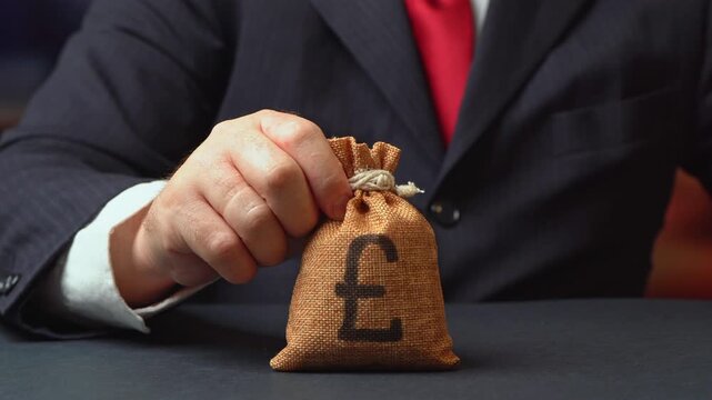 A businessman holds out a British pound money bag. Getting a grant. Mortgage, loan approval. Salary, benefits, profit. Attracting investments. Deposit savings. Banking and crediting. Easy Money.