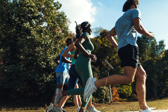 Rear view od diverse group of athletes running together along a sunlit park path during an outdoor marathon competition.