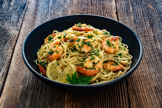 Spaghetti with fried shrimps, olive oil and parsley on wooden table