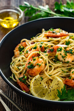 Spaghetti with fried shrimps, olive oil and parsley on wooden table