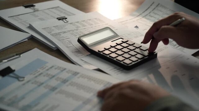 Close-up of hands using calculator on financial reports and spreadsheets, showing budget calculation, accounting analysis and business number review.
