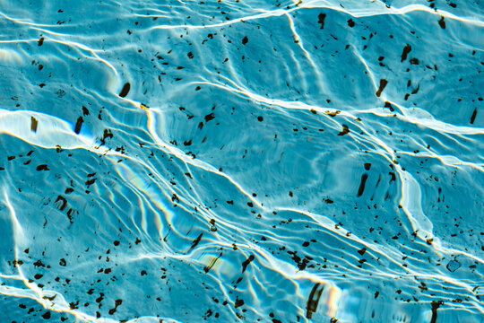 A close-up view of the detailed texture of the water in a pool or fountain, illuminated by the sun's rays	
