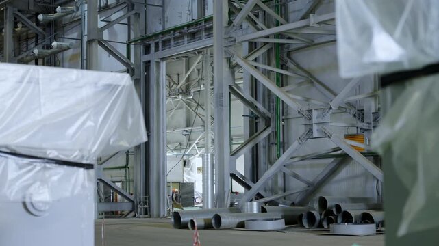 Interior of large industrial building contains sturdy metal structures. Vast manufacturing hall features various construction materials
