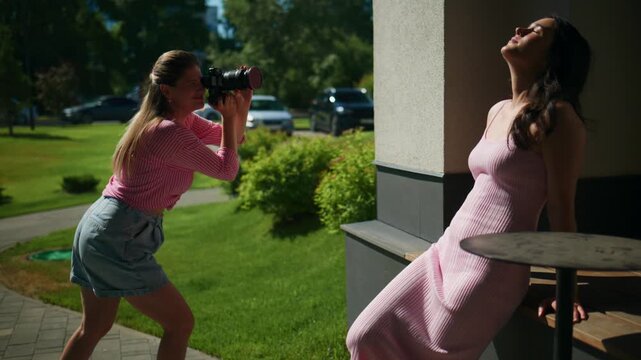 Woman in a pink dress leans on a balcony, basking in sunlight. Photographer captures her in a serene, outdoor setting. The scene suggests a calm, stylish portrait session on a sunny day