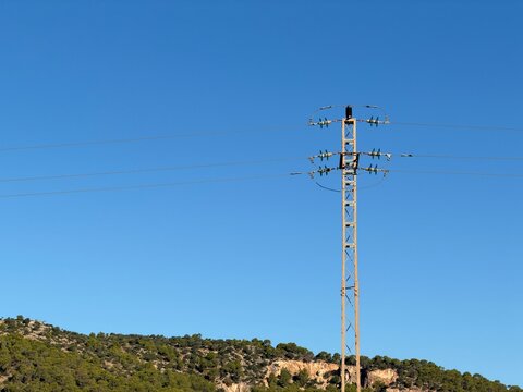 Electricity pylon transmitting power lines against clear blue sky, illustrating energy distribution and infrastructure development in the natural landscape near calvia, balearic islands copy space