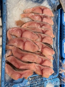 Freshly cut shark meat slices displayed on ice in a blue tray at a bustling fish market in palma, balearic islands, spain, ready for sale to consumers
