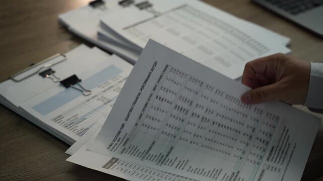 Hands reviewing and turning financial documents on clipboard, showing tax document review, accounting audit workflow and financial report analysis.