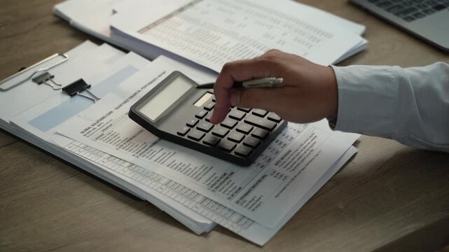 Hands reviewing financial reports and tax documents with pen beside calculator, showing financial audit review, accounting analysis and business reporting.