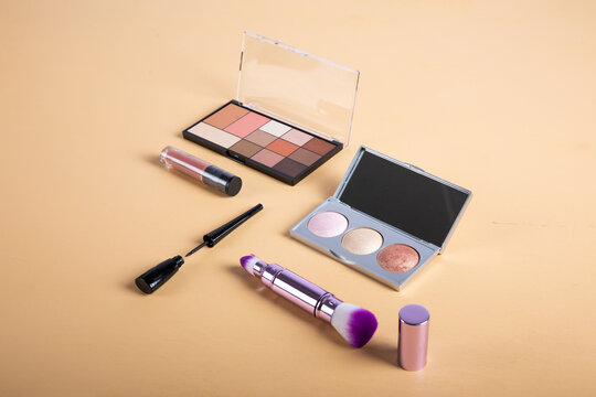 Collection of makeup products including eyeshadow, lipstick, and brushes on a neutral background