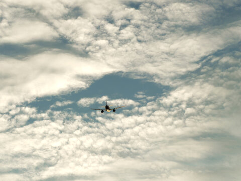 Commercial passenger jet airplane ascending through dramatic partly cloudy blue sky, photographed from ground level below in natural daylight