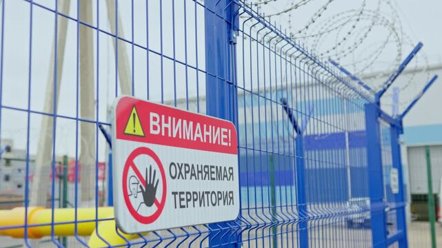 Prominent safety notice hangs on sturdy blue metallic fence. Blue metal sectional fence surrounding specialized gas distribution point