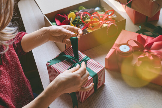 Woman carefully wrapping a gift with paper and ribbon at home.
The scene illustrates gift preparation, personalized shopping, product presentation and consumer gifting for special occasions.