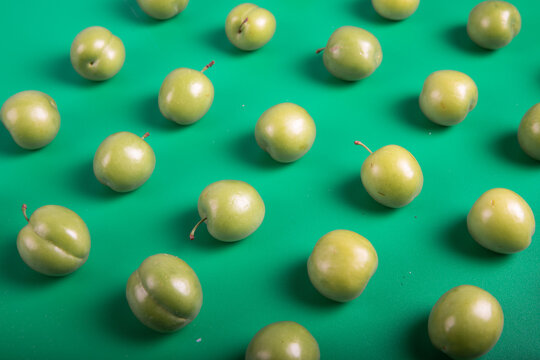 Fresh green plums arranged in a repeating pattern on a vibrant green background