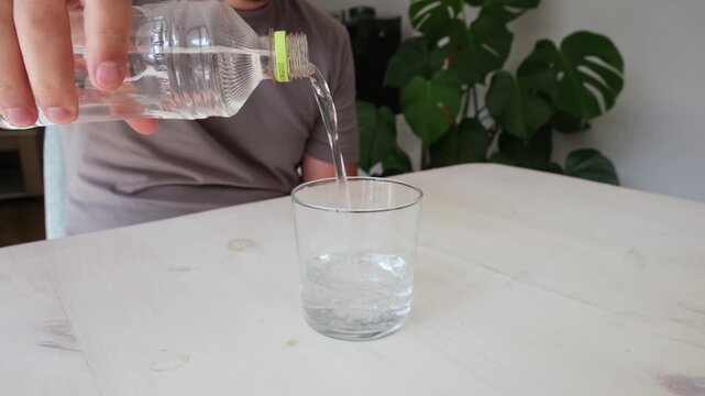 Man's hand pouring clean drinking water from a plastic bottle into a transparent glass at home