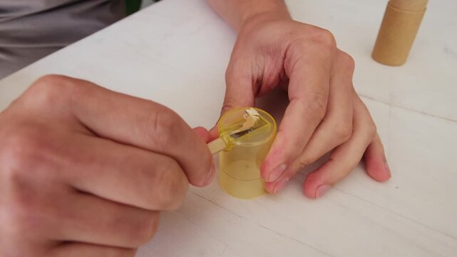 Male hands carefully sharpening a classic wooden pencil with a yellow manual sharpener
