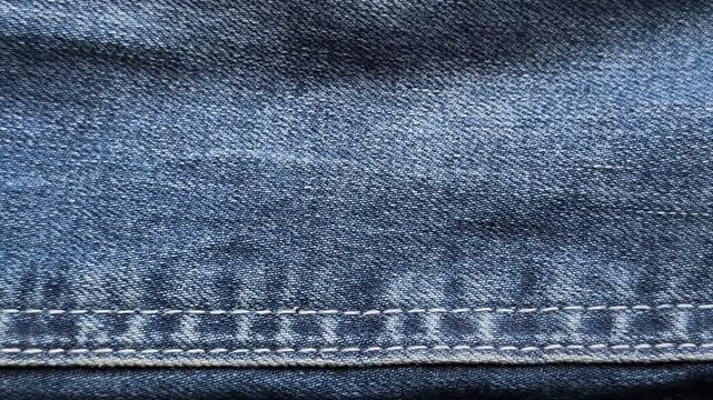 Macro close up of blue denim jeans fabric texture moving along stitched double seam line, revealing detailed cotton weave, thread, and blue denim pattern for fashion, textile, and apparel b-roll.