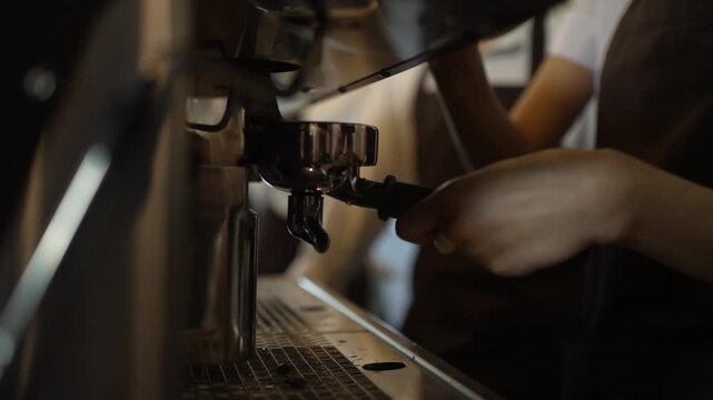 Hands hold portafilter and shot glass at espresso machine in cafe