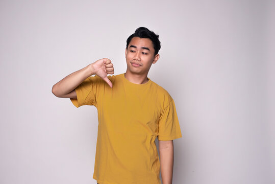 Unhappy Asian man giving thumbs down gesture with negative expression and disapproval standing over isolated white background.