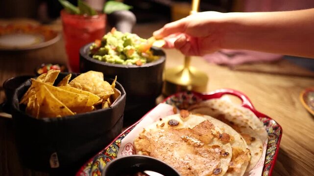 Close up slow motion video of hand dipping tortilla chip into bowl of fresh guacamole.