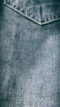 Macro close up of blue faded denim jeans fabric texture smoothly moving upward to reveal back pocket seam stitching, showcasing detailed cotton weave and casual apparel style for fashion.