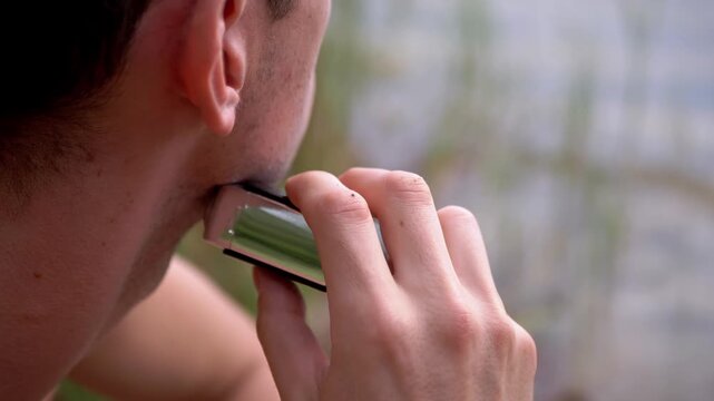 Young man trims his stubble using a metallic electric foil shaver in bright daylight outdoors. The compact grooming device provides smooth tactile cutting against masculine skin.