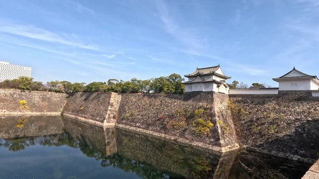 Cinematic wide pan of Osaka Castle moat and historic stone fortifications under clear blue sky in Japan.